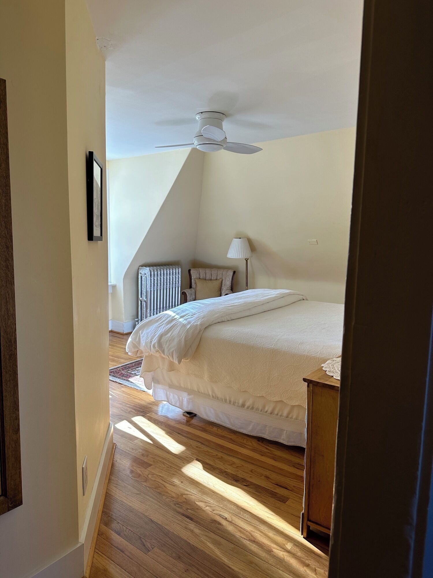 A bedroom with a bed, a radiator, a lamp, and a ceiling fan.