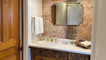 A bathroom with a wooden vanity, a large mirror, a sink with gold fixtures, and two pendant lights.