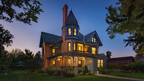 Une grande maison à étages, dotée d’une tour imposante et de nombreuses fenêtres, entourée d’une pelouse bien entretenue.