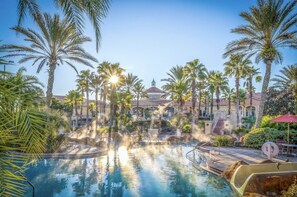 A resort pool with a hot tub, surrounded by palm trees and a building with a red roof. - Disney World Cinderella Castle w/Lazy River, Arcade Games + Family Friendly  (Davenport)