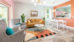 Uma sala de estar com parede quadriculada, um sofá, uma mesa de centro e um espaço de jantar com uma mesa e cadeiras brancas.