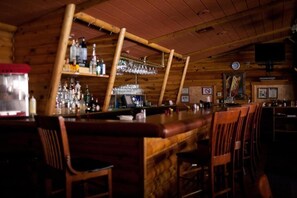 Zona de bar con paredes de madera, una barra y taburetes.