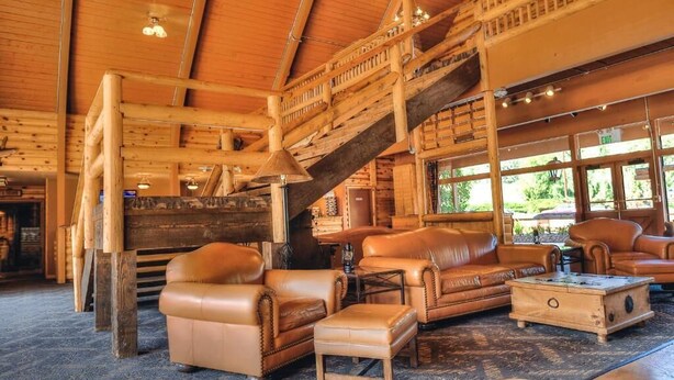 A log cabin interior with leather furniture, a staircase, and large windows. - Payson | Family Nature Retreat | Pool + Hot Tub | 2BR (Payson)