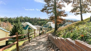 A pathway leading to a row of cabins with green roofs, surrounded by trees and a hilly landscape.