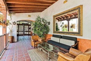 A spacious lobby with a tiled floor, a sofa, leather armchairs, a glass coffee table, and a large mirror.
