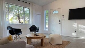 En moderne stue med et stort vindue, et fladskærms-tv, to sorte stole, et rundt træbord og en grå sofa.