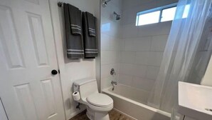 Ein Badezimmer mit Toilette, Badewanne und Dusche. Zwei Handtücher hängen an der Wand.