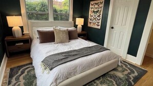 Ein Schlafzimmer mit einem großen Bett, zwei Nachttischlampen, einem Fenster, einer Tür und einem Wandbild.