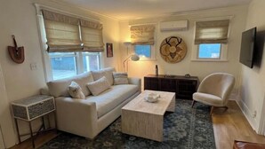 Ein Wohnzimmer mit Sofa, Couchtisch und Sesseln, einem gemusterten Teppich und einem Fernseher an der Wand.