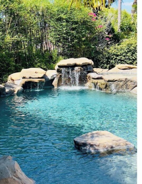 A clear pool with a waterfall feature surrounded by rocks and lush greenery.