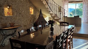A dining area with a long wooden table and chairs, a stone wall, and a staircase leading to a balcony.