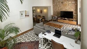 A spacious living area with a high ceiling, a stone wall, a large flat-screen TV, and a dining area with a patterned floor. - Newly designed 3BR apartment + Private terrace (Ciudad de Panamá)