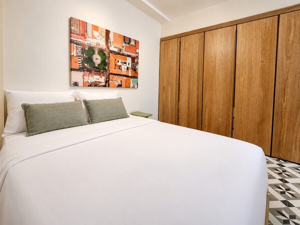 A bedroom with a bed, a wooden wardrobe, and a cityscape artwork on the wall.