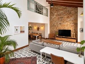 A modern living room with a stone wall, a flat-screen TV, a dining area, and a staircase.