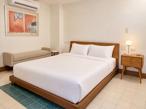 A hotel room with a large bed, a bedside table with a lamp, a small round table, and a sofa.