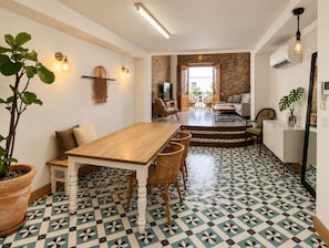 A dining area with a wooden table and chairs, a potted plant, and a patterned floor.