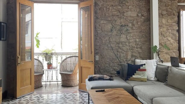 A living room with a stone wall, a wooden door, a sofa, a coffee table, and a patterned floor. - Newly designed 3BR apartment + Private terrace (Ciudad de Panamá)
