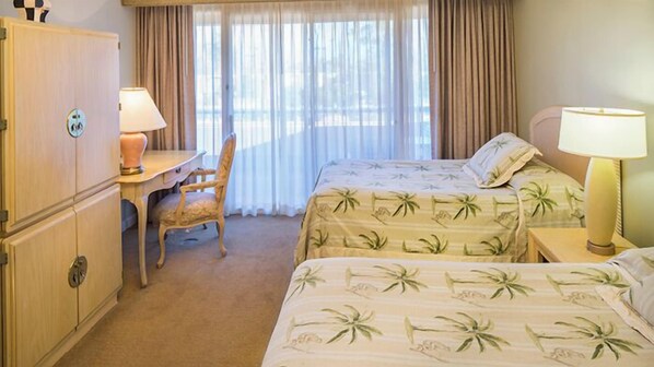 Habitación de hotel con escritorio, dos camas con cubrecamas florales, una silla y un armario.