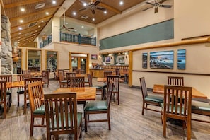 A spacious restaurant with wooden tables and chairs, a balcony, and artwork on the walls.