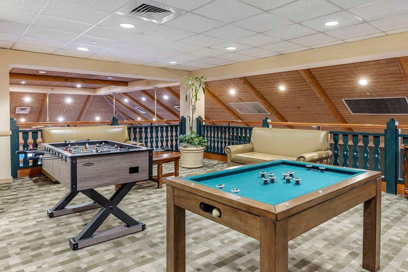 A pool table, foosball table, and a sofa in a room with wooden beams and a sloped ceiling.
