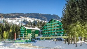 A hotel with multiple floors, a ski slope in the background, and a clear sky. - Schladming | Couples Ski Stop | Pool + Spa (Schladming)