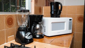 Una cocina con licuadora, cafetera y microondas sobre una encimera azulejada.