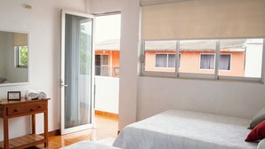 Habitación de hotel con dos camas, una mesita de noche de madera, un espejo y una ventana con vistas a edificios.