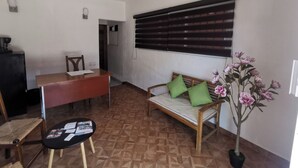 Una habitación con un sofá de madera, una mesita, un ventilador de techo, una ventana con persianas y una planta en maceta.