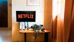 Una habitaci ón con un escritorio de madera, un cartel enmarcado de flores y un cartel grande que dice "NETFLIX".