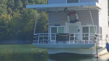 Enjoy a tranquil stay on this houseboat, featuring a spacious balcony with a lifebuoy and a small deck area perfect for outdoor activities amidst lush surroundings.