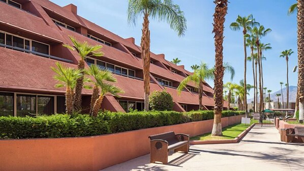 Un edificio moderno con fachada roja, rodeado de palmeras y un jardín cuidado.