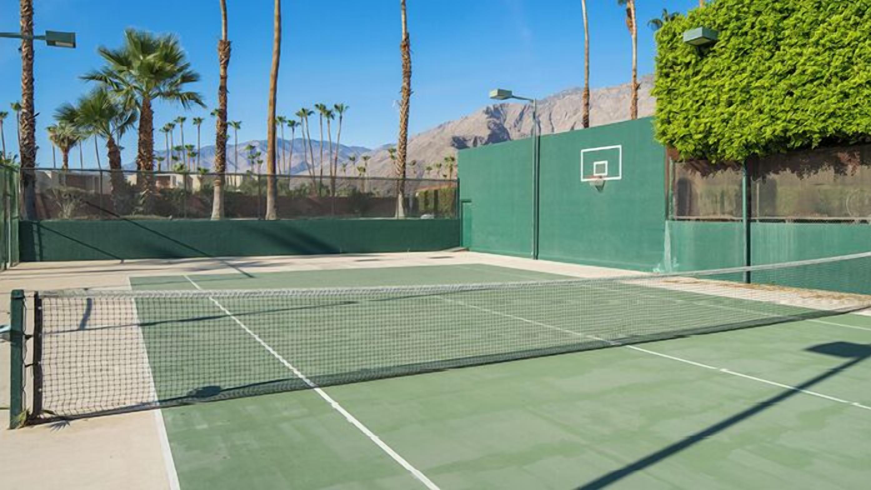 Un court de tennis doté d’une surface verte, entouré de palmiers et avec une montagne en arrière-plan.