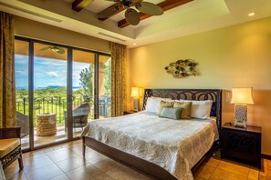 Un dormitorio con una cama grande, un ventilador de techo, vistas al exterior y una mesita de noche con lámpara.