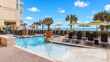 A pool area with lounge chairs and umbrellas, overlooking a beach.