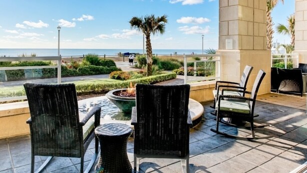 An outdoor patio with wicker chairs, a small fire pit, and a view of the sea. - Virginia Beach | Ocean View Balcony Stay | Pool & Beach | Studio (Virginia Beach)