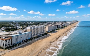 Een kusthotel met meerdere verdiepingen, een strandboulevard en een steiger die in de oceaan uitloopt.