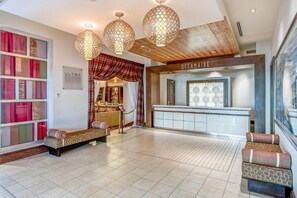 A hotel lobby with a reception desk, a seating area, and a large window with curtains.