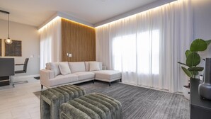 A modern living room with a sectional sofa, a grey rug, and a large window with white curtains.