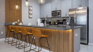 A modern kitchen with a central island, bar stools, stainless steel appliances, and pendant lighting.