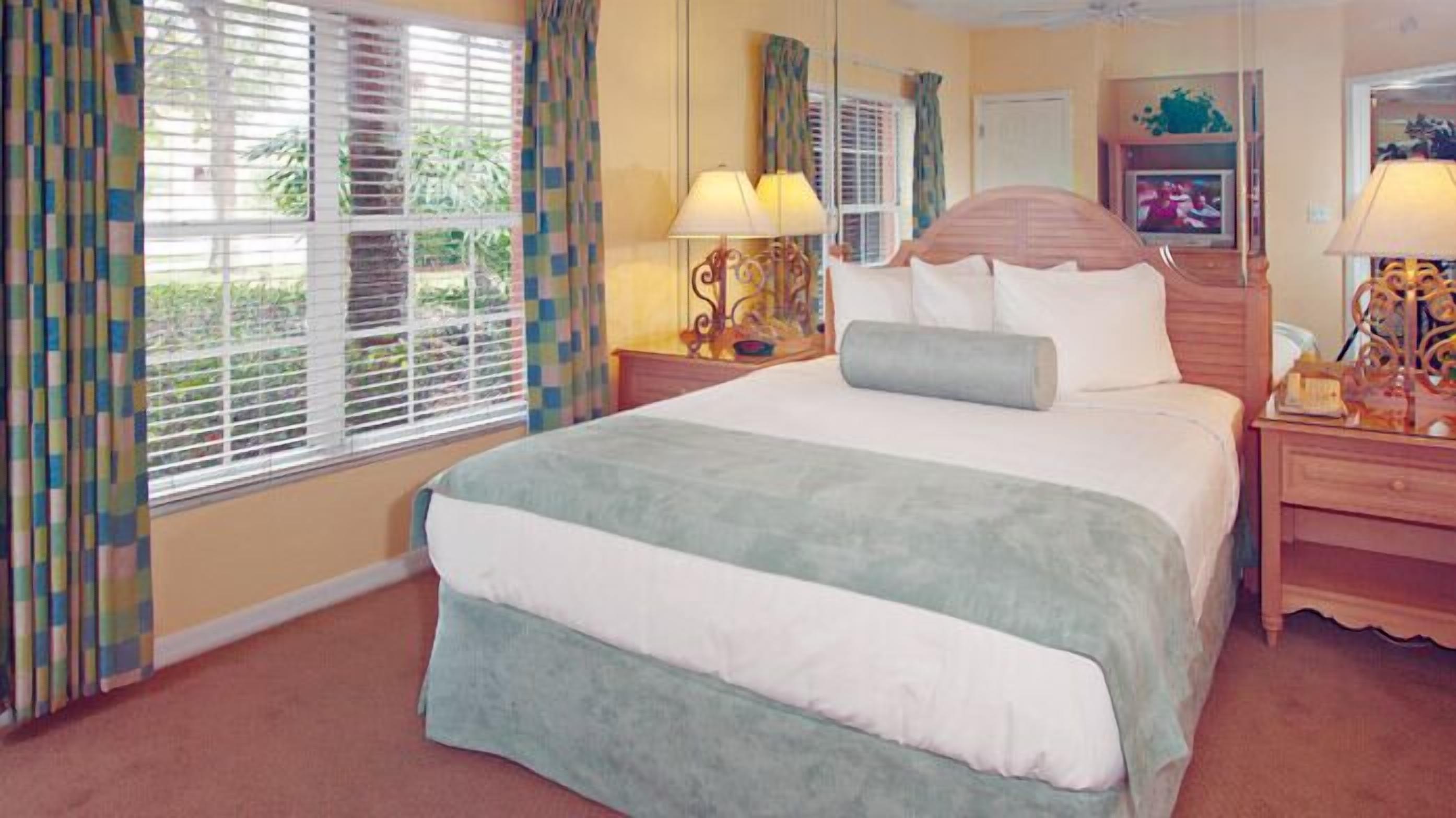 Una habitación de hotel con una cama grande, dos lámparas de noche, una mesita de madera y una ventana con persianas.