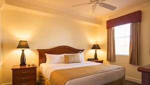 Une chambre d’hôtel avec un lit, deux tables de chevet, des lampes, un ventilateur de plafond et une fenêtre avec des rideaux.