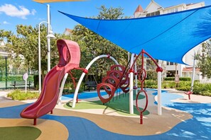 A playground with a slide and climbing structures, surrounded by greenery and a blue canopy. - Grand Beach - 3 Bedroom Full Mobility - Phase I (Orlando)