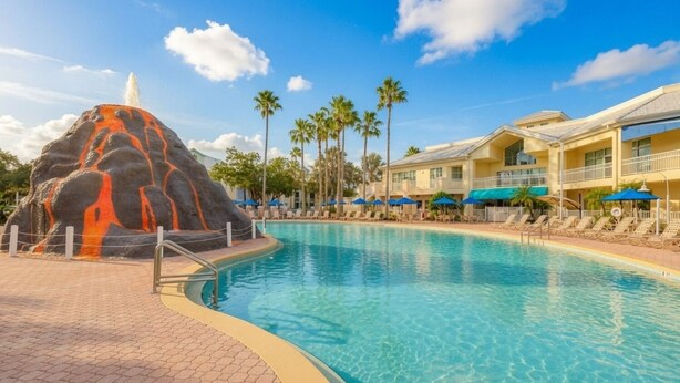 A pool with a rock feature, palm trees, and a hotel with multiple balconies. - Orlando | Family Orlando Park Getaway | Pool + Hot Tub | 2BR Condo (Orlando)