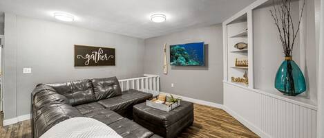 A modern living room with a sectional sofa, a coffee table, and a decorative wall with a 'gather' sign.