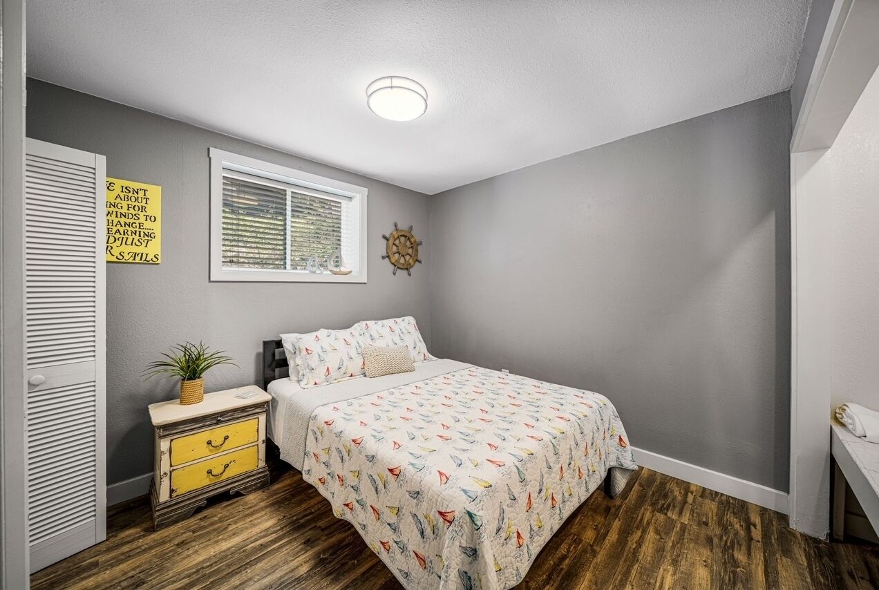 A bedroom with a bed, a nightstand, a window, and a wall clock.