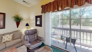 A living room with a leather recliner, a sofa, a potted plant, and a large window with a view of the outdoors. - Sea Trail Sunset Beach | Golf, Beach & Relaxation | RP 2605 (Sunset Beach)