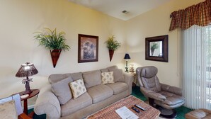 A living room with a sofa, armchair, and two potted plants. There is a lamp, a framed picture, and a window with curtains. - Sea Trail Sunset Beach | Golf, Beach & Relaxation | RP 2605 (Sunset Beach)