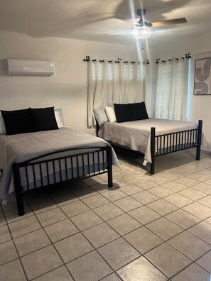Two single beds with black frames and white bedding, a ceiling fan, and a wall-mounted air conditioner.
