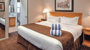 A hotel room with a bed, a nightstand, a lamp, a framed picture on the wall, and a bathroom visible through an open door. - Pinetop | Family Cabin Retreat |  local hikes | 2BR (Pinetop)