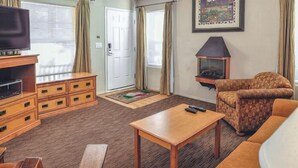 A living room with a TV, wooden furniture, a patterned armchair, and a fireplace. - Pinetop | Family Cabin Retreat |  local hikes | 2BR (Pinetop)